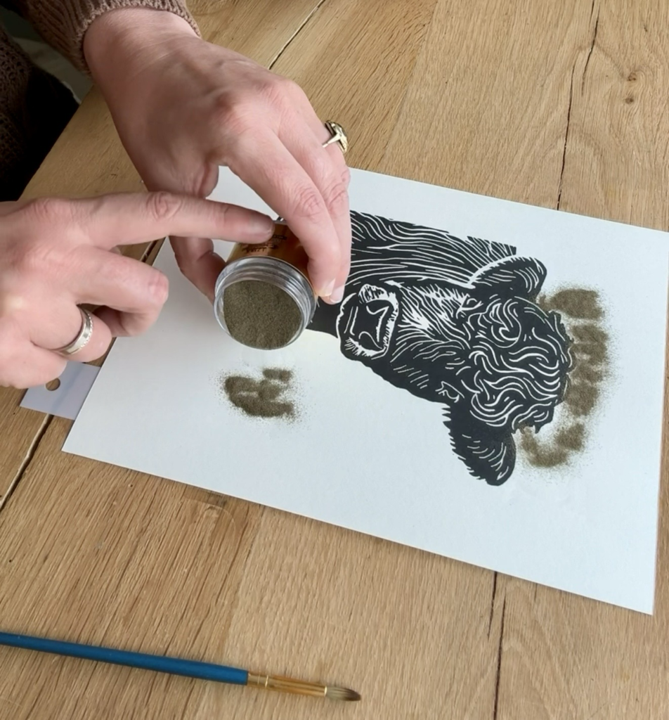 Sprinkling gold embossing powder onto the Holy Cow linoprint